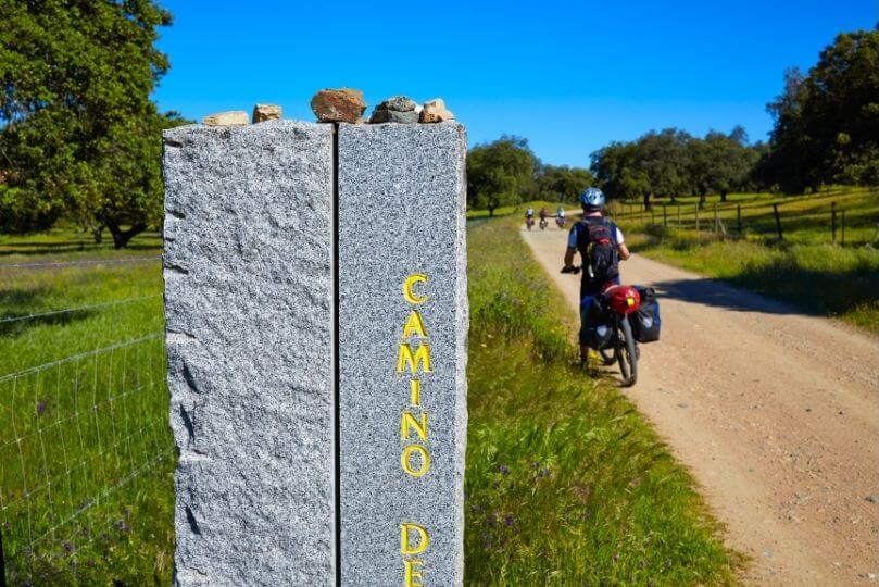 Pellegrino in bici vicino a pilastro che indica il cammino di santiago